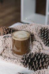 New Year, Christmas card. Coffee with milk in a glass mug among the cones on the blanket. Vertical photo
