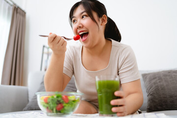 Beautiful Asian woman eating salad, holding a glass bowl and using a fork to pick up a tomato to eat