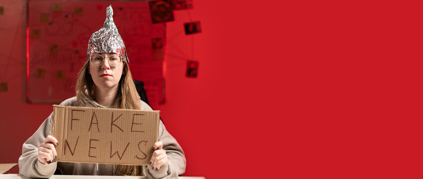 Female conspiracy theorist in protective foil cap and glasses debunks myths holding poster fake news. Conspiracy theory concept. The schizophrenic works. Banner.