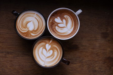 Three Cups of Coffee with Beautiful Latte Art Designs on a Wooden Table, Highlighting Craftsmanship and Coffee Culture