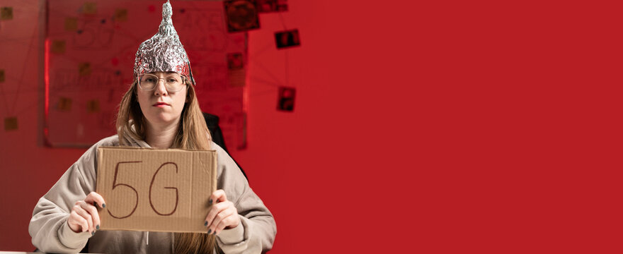 Female conspiracy theorist in protective foil cap and glasses debunks myths holding poster 5G. Conspiracy theory concept. The schizophrenic works. Banner.