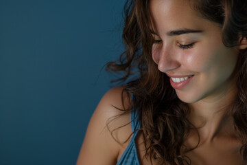 Portrait photo of a latina hispanic female model looking down at something with a smiling face isolated on a blue background