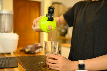 Young woman pouring a chocolate protein shake into a glass. Healthy drinking and nourishment concept