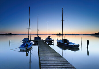 Wooden Pier by calm lake with boats before sunrise at dawn
