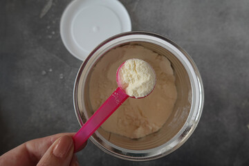 Woman holding a scoop of supplemental nutrition drink powder above an open container
