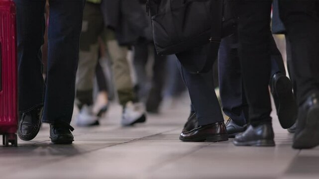 Low shot of legs and feet of people walking in a crowded Tokyo subway train station as a red suitcase rolls by during rush hour in slow motion circa 2024. Captured at 120 frames per second.

