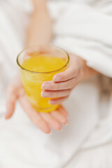 Woman holding cup of orange juice in bed with white sheet, blanket, and pillow