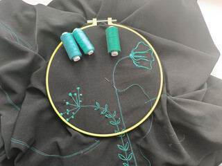 The process of embroidering flowers with green threads on black fabric