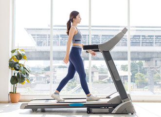 Full body asian young beautiful cheerful happy woman, active sport girl in sportswear exercise running jogging on treadmill training in fitness gym or living room at home, healthy wellness lifestyle.