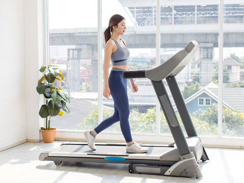 Full body asian young beautiful cheerful happy woman, active sport girl in sportswear exercise running jogging on treadmill training in fitness gym or living room at home, healthy wellness lifestyle.