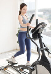 Asian young beautiful cheerful happy woman active girl in sportswear stationary exercise bike movement speed energy training in fitness gym or living room at home, healthy wellness action lifestyle