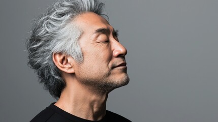 Fototapeta premium Photo of a mature, handsome Japanese man with gray hair, eyes closed in profile view on a gray background, with side lighting.generated ai 