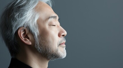 Fototapeta premium Photo of a mature, handsome Japanese man with gray hair, eyes closed in profile view on a gray background, with side lighting.generated ai 