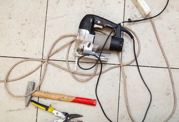 A corded power tool is laying on the floor next to a hammer