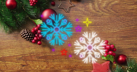 Image of neon snowflake icons over christmas decorations on wooden surface with copy space