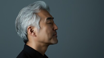 Photo of a mature, handsome Japanese man with gray hair, eyes closed in profile view on a gray background, with side lighting.generated ai	