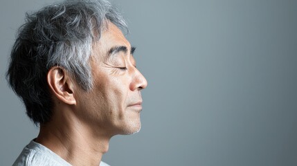 Fototapeta premium Photo of a mature, handsome Japanese man with gray hair, eyes closed in profile view on a gray background, with side lighting.generated ai 