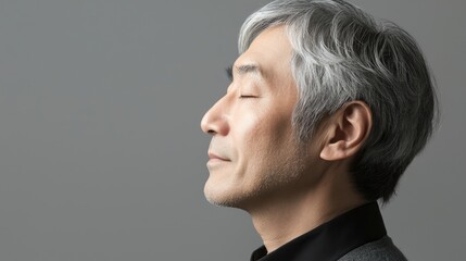 Obraz premium Photo of a mature, handsome Japanese man with gray hair, eyes closed in profile view on a gray background, with side lighting.generated ai 