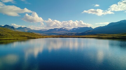 Fototapeta premium Serene lake reflecting mountains and clouds under a clear blue sky.