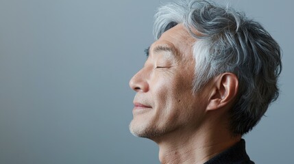 Fototapeta premium Photo of a mature, handsome Japanese man with gray hair, eyes closed in profile view on a gray background, with side lighting.generated ai 