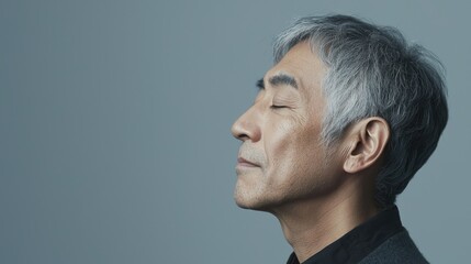 Fototapeta premium Photo of a mature, handsome Japanese man with gray hair, eyes closed in profile view on a gray background, with side lighting.generated ai 