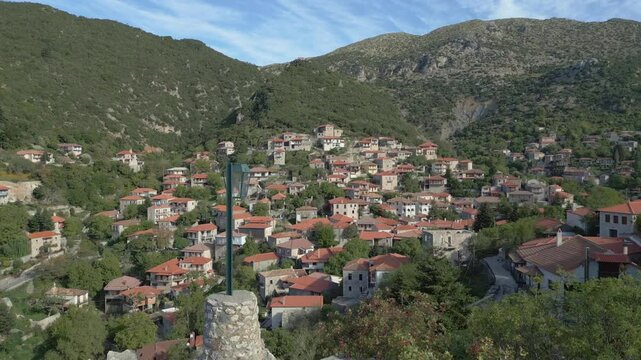 A vertical drone takeoff in front of Stemnitsa traditional village, revealing its picturesque stone-built houses nestled among lush green hills and rugged mountain scenery