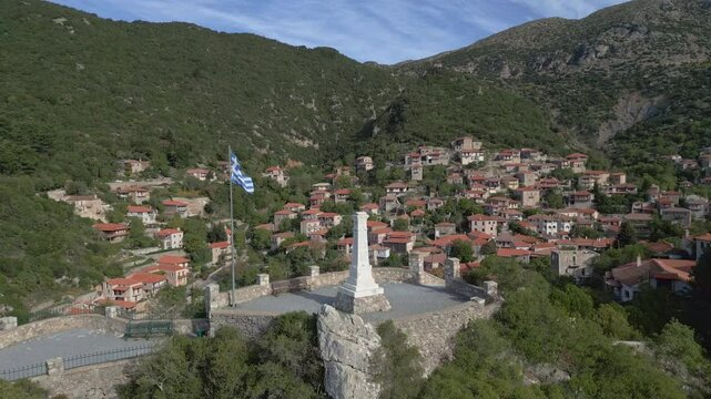 Capture with a drone an orbit of the Stemnitsa Monument of 1940, showcasing the traditional village beautifully framed in the background
