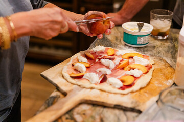 Assembling a pizza with prosciutto, peaches, and ricotta cheese