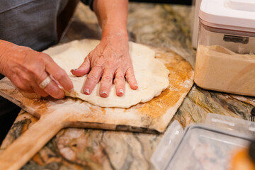 Shaping pizza dough with hands on a flour-dusted wooden paddle