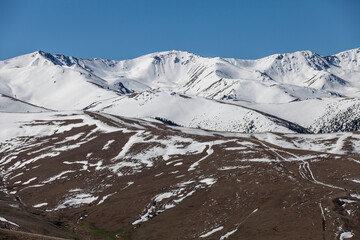Snow-capped mountains and partially thawed terrain under blue sk