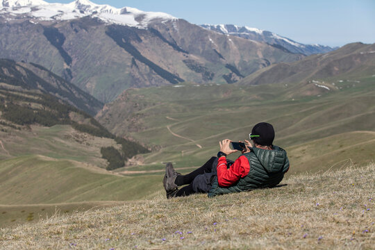 Person taking photo of mountain landscape while lying down on gr