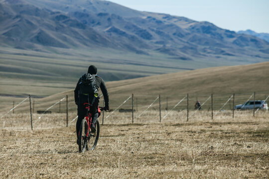Cyclist Riding Through Dry Grassland with Mountainous Background