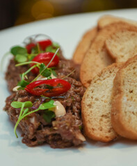 Beef tartar with red pepper and toast on a white plate