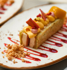 Fruit cake with orange, mango and strawberry sauce on a white plate