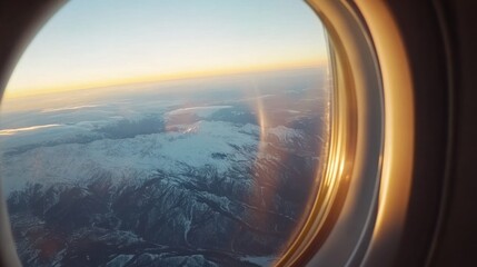View from an airplane window overlooking snowy mountains at sunset.