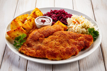 Crispy breaded fried pork chop, fried potatoes, ketchup and red and white cabbage served on white...