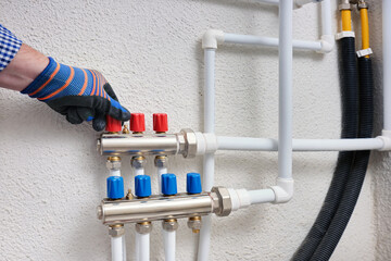 A plumber adjusts the hot water supply manifold valves in the heating system of an apartment or...