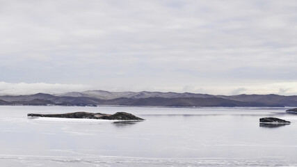 Expansive frozen surface of Lake Baikal in winter, with an isolated rock formation and distant hills visible.