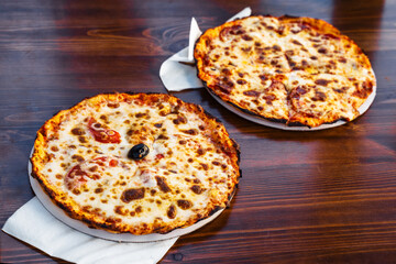 Freshly baked cheese and pepperoni pizzas served on a wooden table