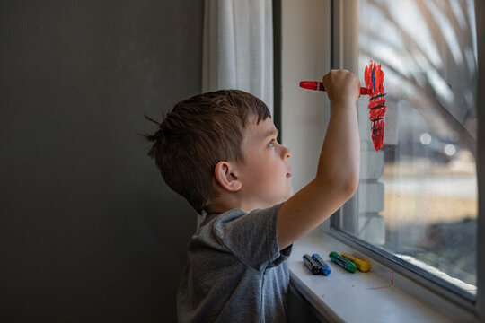 boy drawing on window with crayons with sunlit background