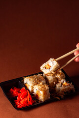 Chopsticks taking portion of sushi roll. Sushi rolls with salmon cream cheese and cucumber in take away package. Food delivery concept.