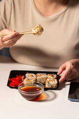 Woman eating sushi rolls with chopstiks at workplace. Healthy asian food during lunch break at work. Sushi in take away package. Tasty asian food