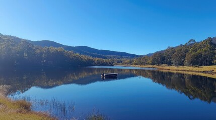 Fototapeta premium A serene lake surrounded by mountains with a small boat floating on the water, reflecting the clear blue sky and surrounding trees. This peaceful outdoor scene is perfect for content on nature, 