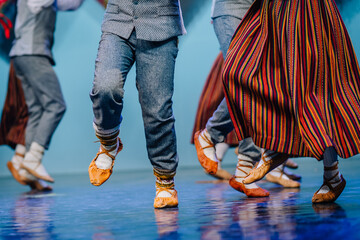  Close-up of dancers’ feet in Latvian Folk dance, wearing traditional leather shoes and colorful striped skirts on a stage floor.