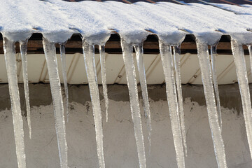 Sharp icicles and melted snow hanging from eaves of roof. Beautiful transparent icicles slowly gliding of a roof