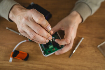 Person using screwdriver for electronic device on wooden surface.