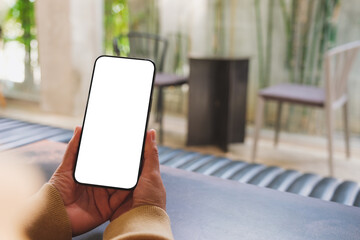 Mockup image of a woman holding and using mobile phone with blank desktop in cafe