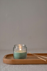 Scented green candle with soft dim light on wooden tray on table, empty neutral taupe gray beige...