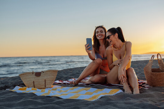 Two women laughing on a beach at sunset