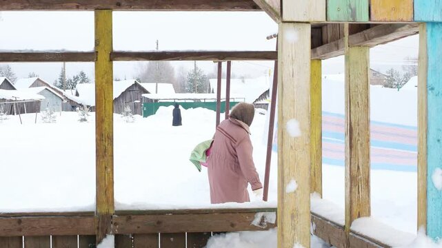 Grandmother gray downy shawl, felt boots goes hang out laundry washing cold. Clean sheets, freshness winter snow outback, traditional daily life far from civilization, wooden village Russia, Siberia